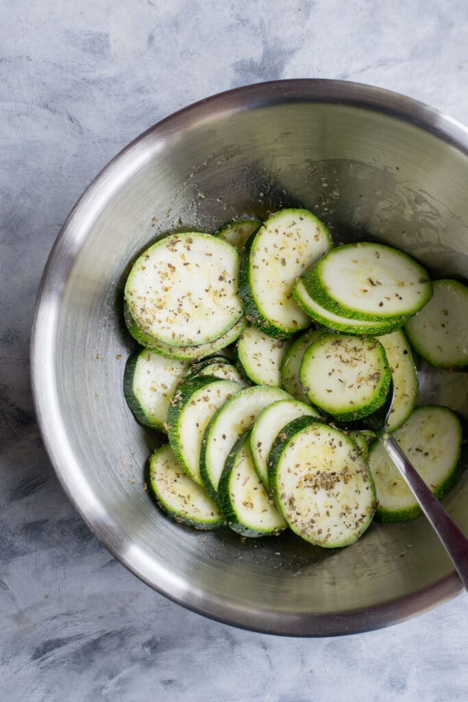 Sliced courgettes in a bowl with olive oil and spices