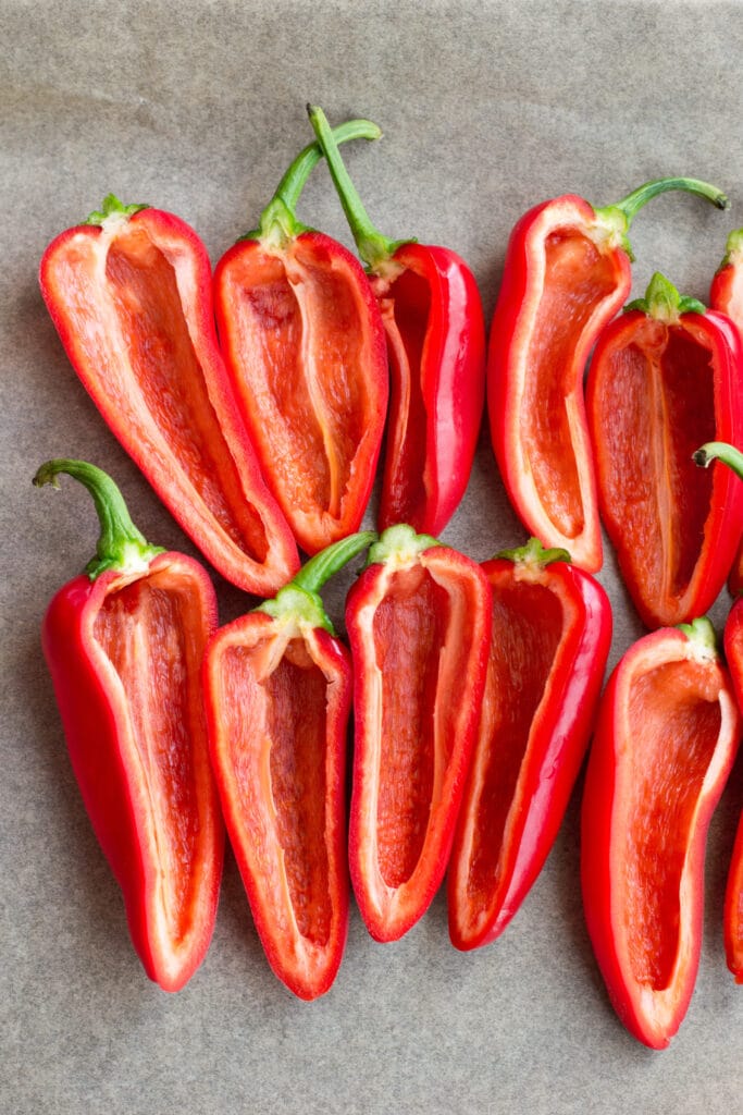 Mini red peppers cut lenghtwise on a baking tray